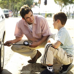 Young Man Checking the Air Pressure of Car Tire with His Son --- Image by © Royalty-Free/Corbis